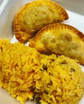 Two golden fried turnovers served beside seasoned yellow rice.