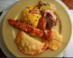 Puerto Rican festival sampler with seasoned rice, roasted meats, a skewer, fried plantain, and a fried turnover.